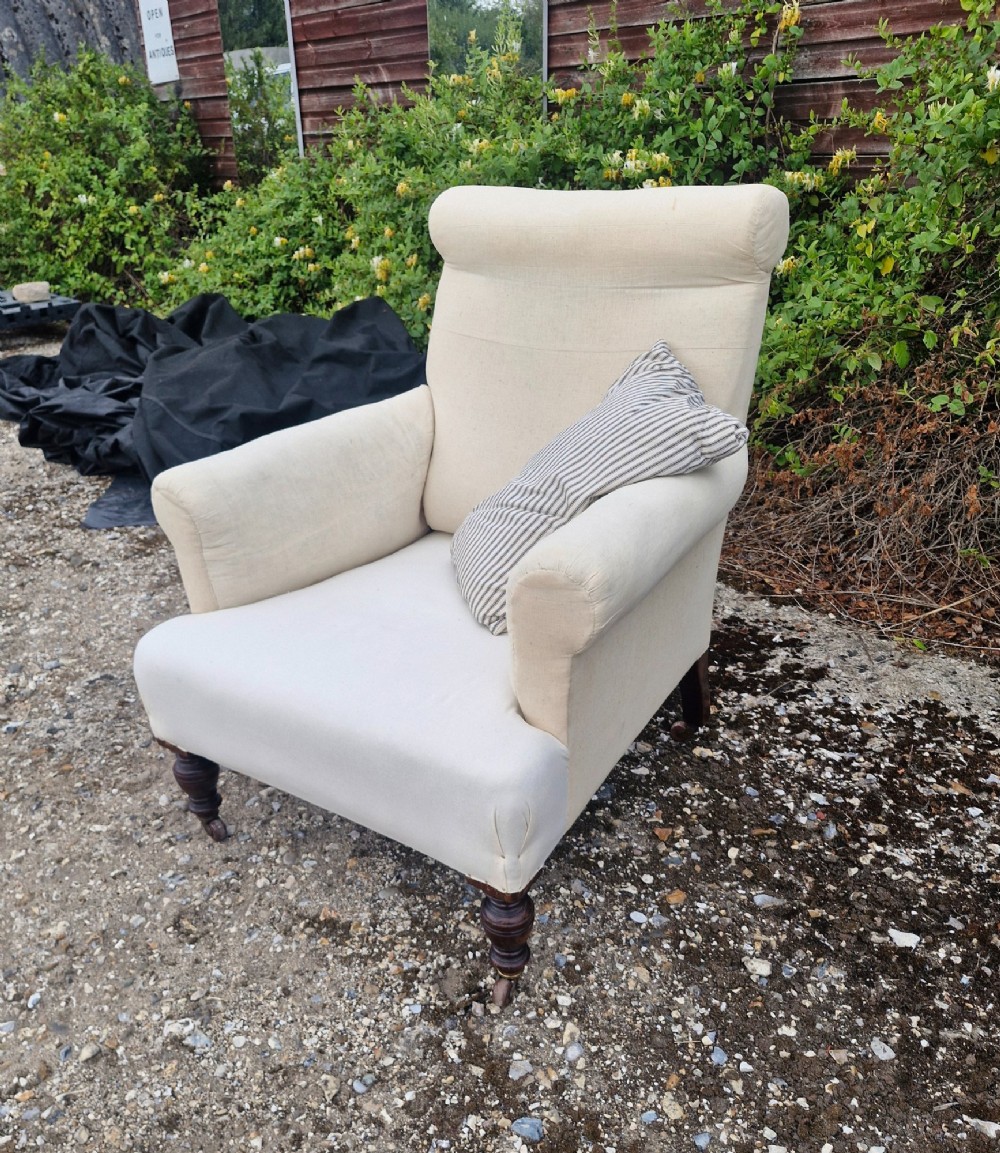 A late Victorian upholstered armchair in neutral cream fabric featuring a scrolled backrest, padded armrests, and turned mahogany front legs on brass castors. View IV
