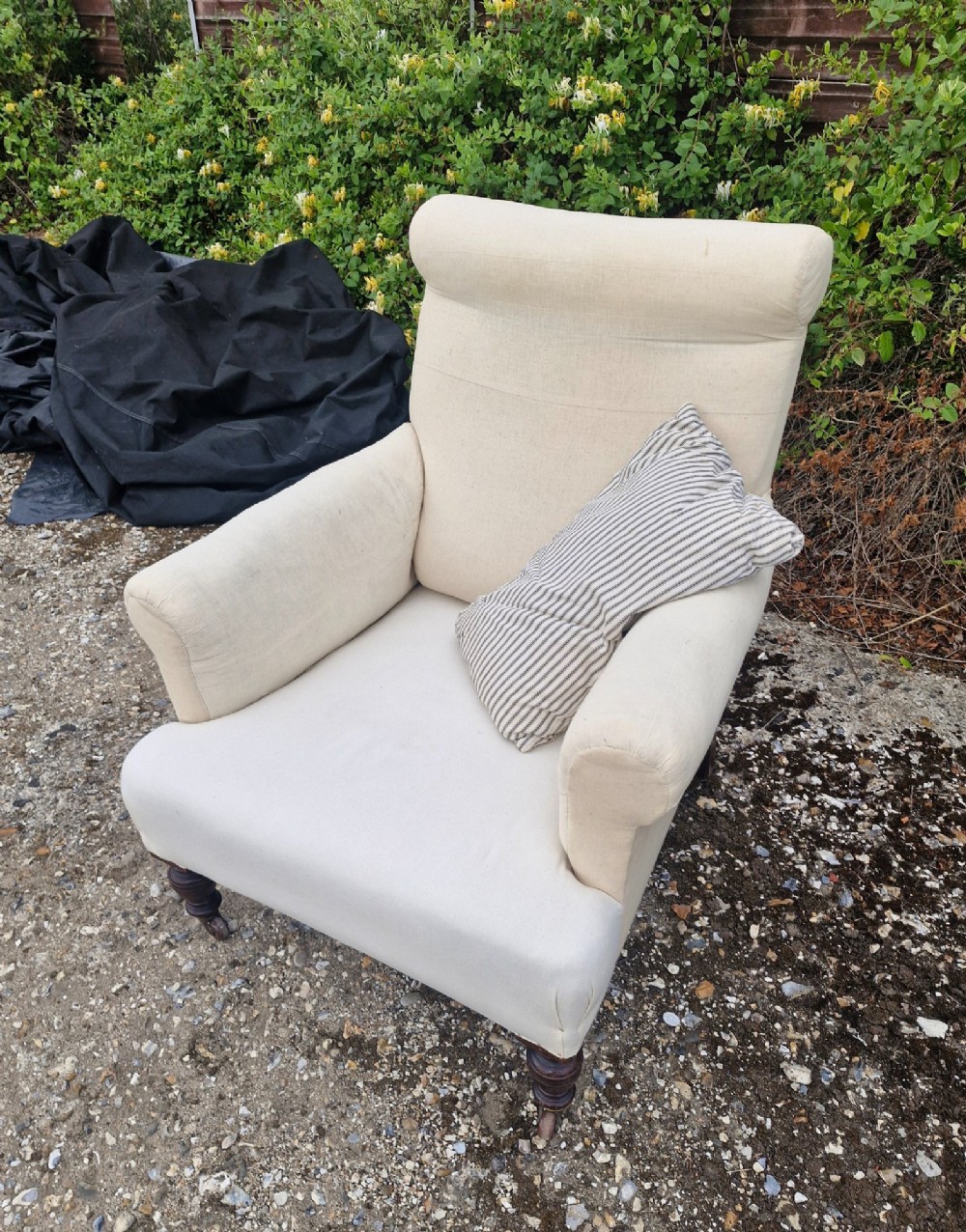 A late Victorian upholstered armchair in neutral cream fabric featuring a scrolled backrest, padded armrests, and turned mahogany front legs on brass castors. View V