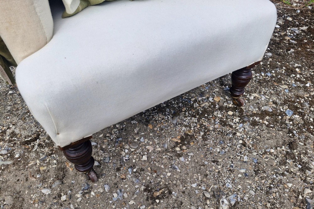A late Victorian upholstered armchair in neutral cream fabric featuring a scrolled backrest, padded armrests, and turned mahogany front legs on brass castors. View VI