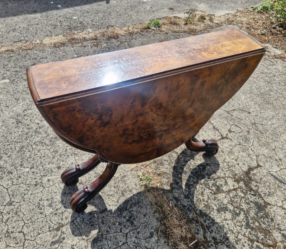 A Victorian burr walnut scissor action table featuring a shaped oval top with distinct figure grain and carved cabriole legs with a central turned stretcher finial. View V