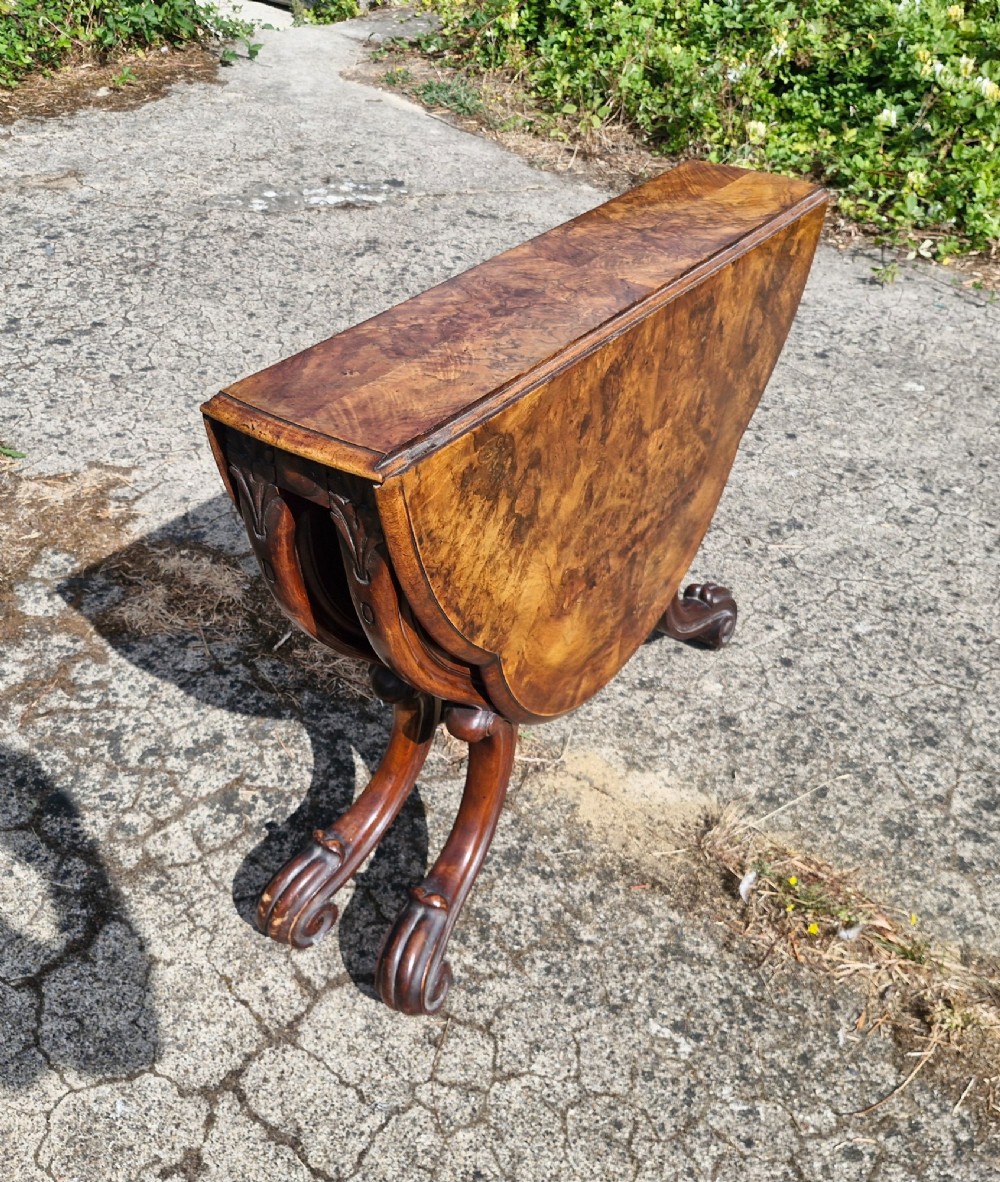 A Victorian burr walnut scissor action table featuring a shaped oval top with distinct figure grain and carved cabriole legs with a central turned stretcher finial. View VI