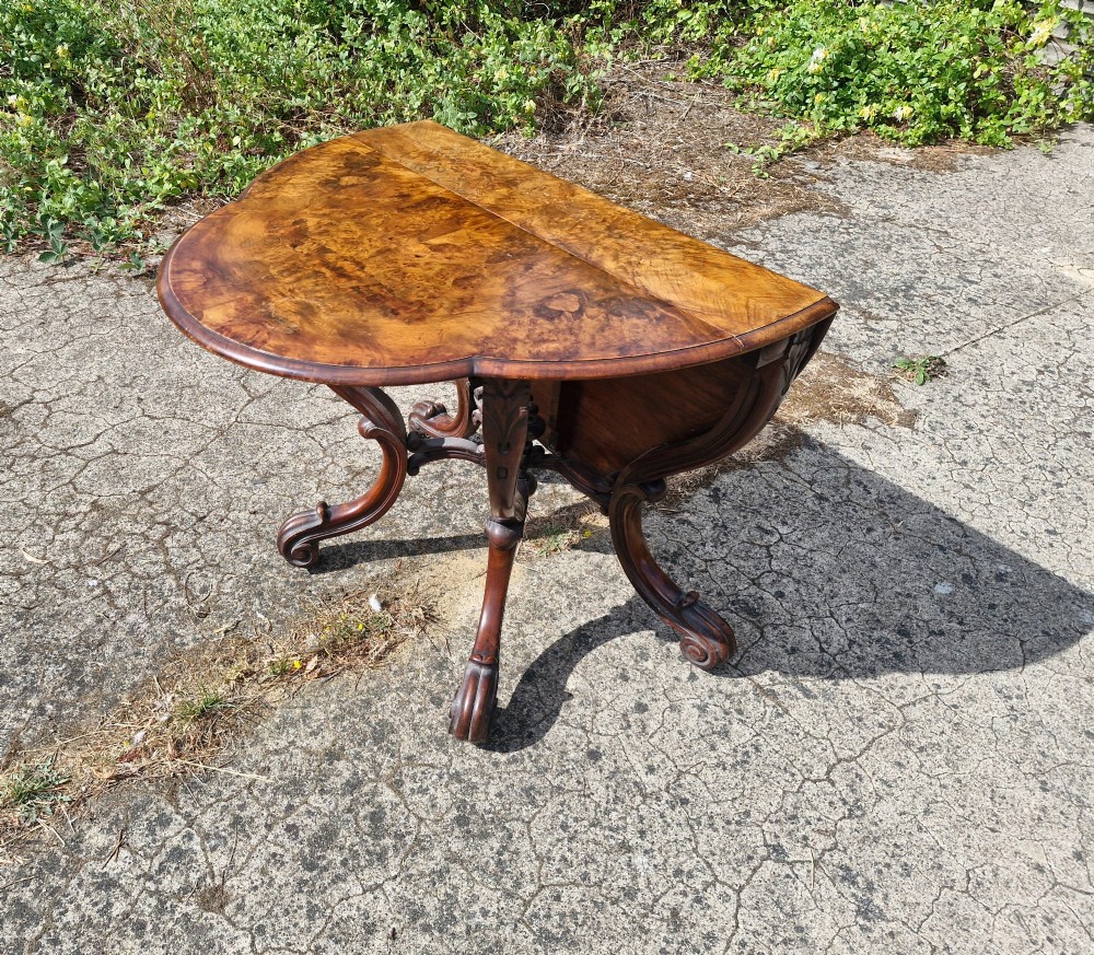 A Victorian burr walnut scissor action table featuring a shaped oval top with distinct figure grain and carved cabriole legs with a central turned stretcher finial. View X
