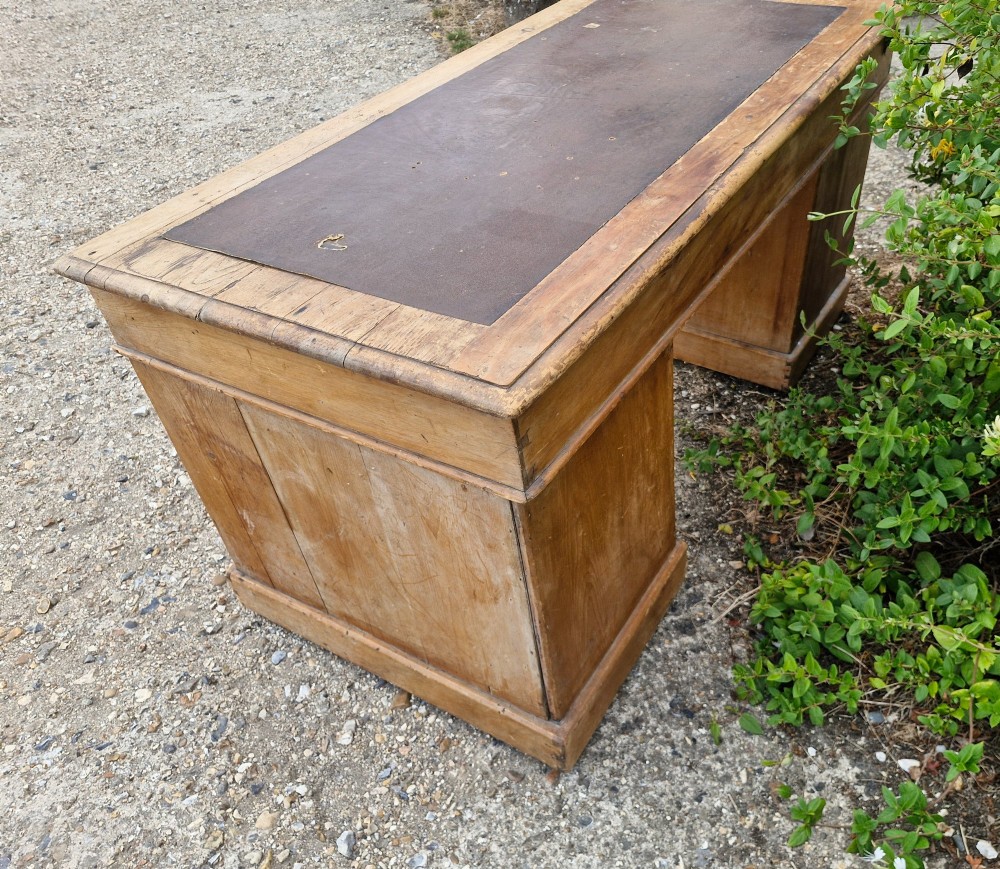 A 19th-century pine kneehole pedestal writing desk featuring a brown leather inset writing surface, nine drawers with brass ring pulls, and a plinth base. View II
