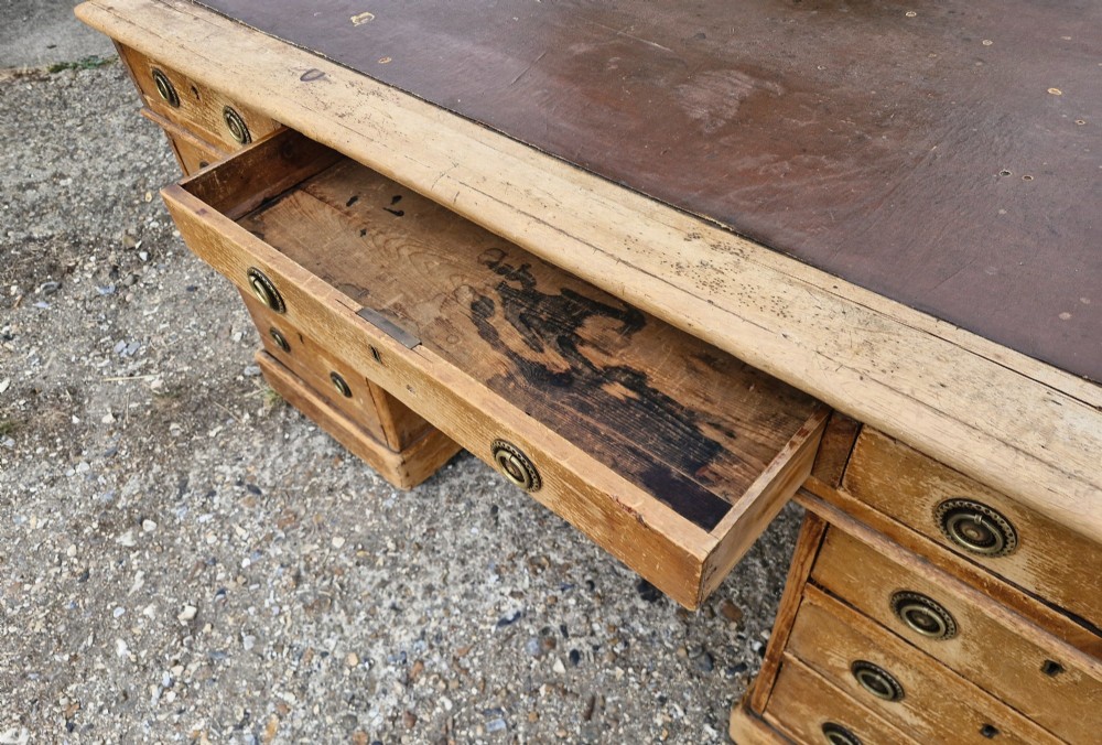 A 19th-century pine kneehole pedestal writing desk featuring a brown leather inset writing surface, nine drawers with brass ring pulls, and a plinth base. View III