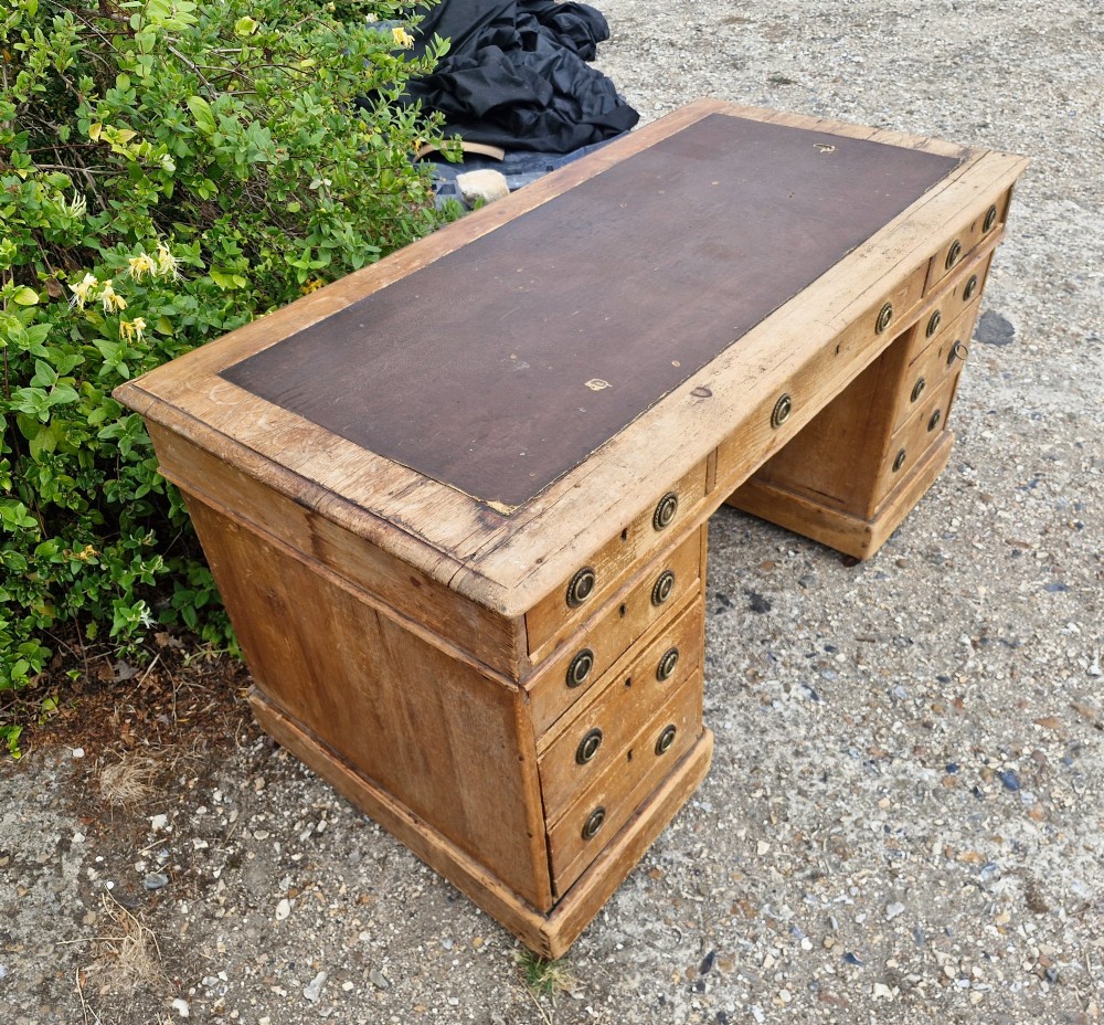 A 19th-century pine kneehole pedestal writing desk featuring a brown leather inset writing surface, nine drawers with brass ring pulls, and a plinth base. View IV