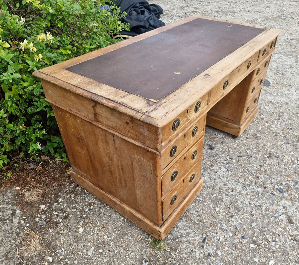 A 19th-century pine kneehole pedestal writing desk featuring a brown leather inset writing surface, nine drawers with brass ring pulls, and a plinth base. View V