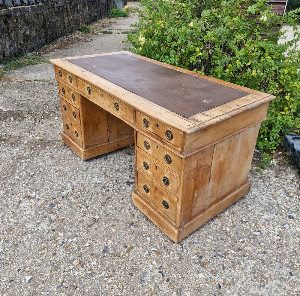 A 19th-century pine kneehole pedestal writing desk featuring a brown leather inset writing surface, nine drawers with brass ring pulls, and a plinth base. View VI