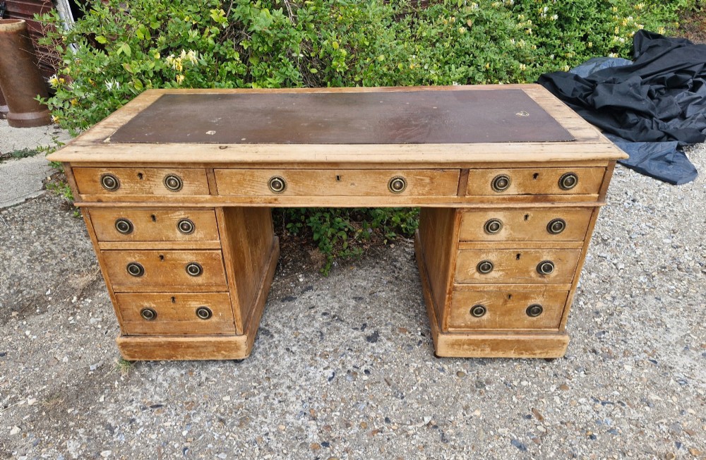 A 19th-century pine kneehole pedestal writing desk featuring a brown leather inset writing surface, nine drawers with brass ring pulls, and a plinth base. View VII