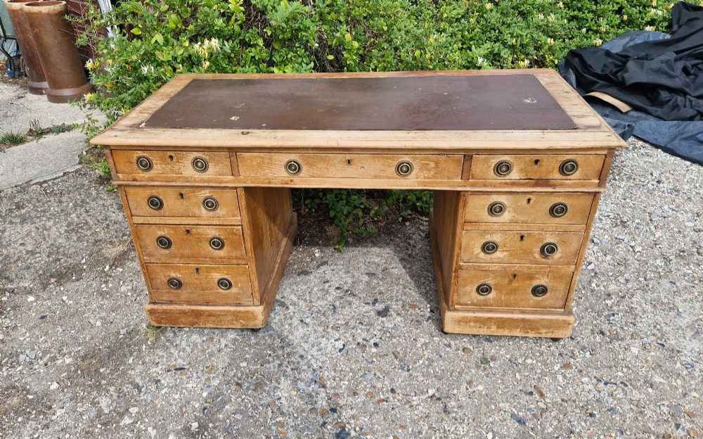 A 19th-century pine kneehole pedestal writing desk featuring a brown leather inset writing surface, nine drawers with brass ring pulls, and a plinth base. View VIII