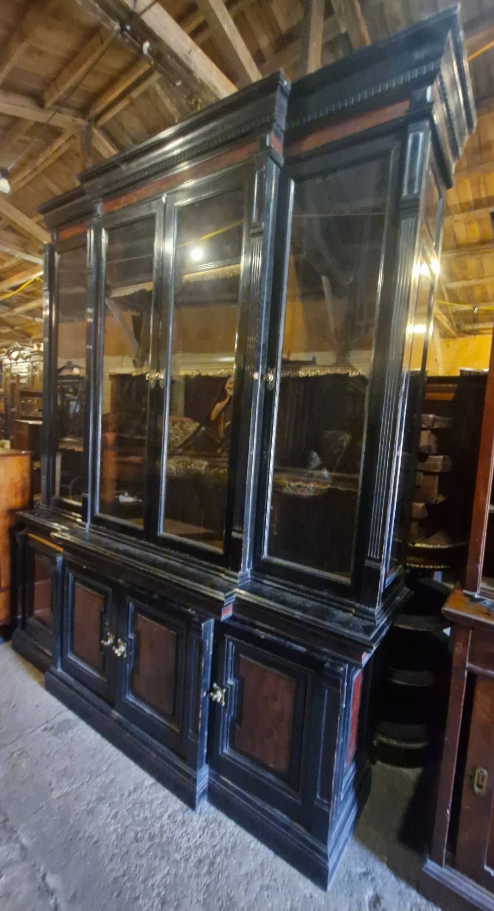 A large Victorian ebonised and mahogany breakfront library bookcase featuring glazed upper doors, panelled lower cupboards, and fluted side pilasters. View II