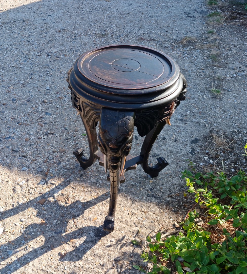 A late Victorian ebonised wood tripod side table featuring three carved elephant heads whose trunks extend to form table legs, set with light-coloured wooden tusks. View II