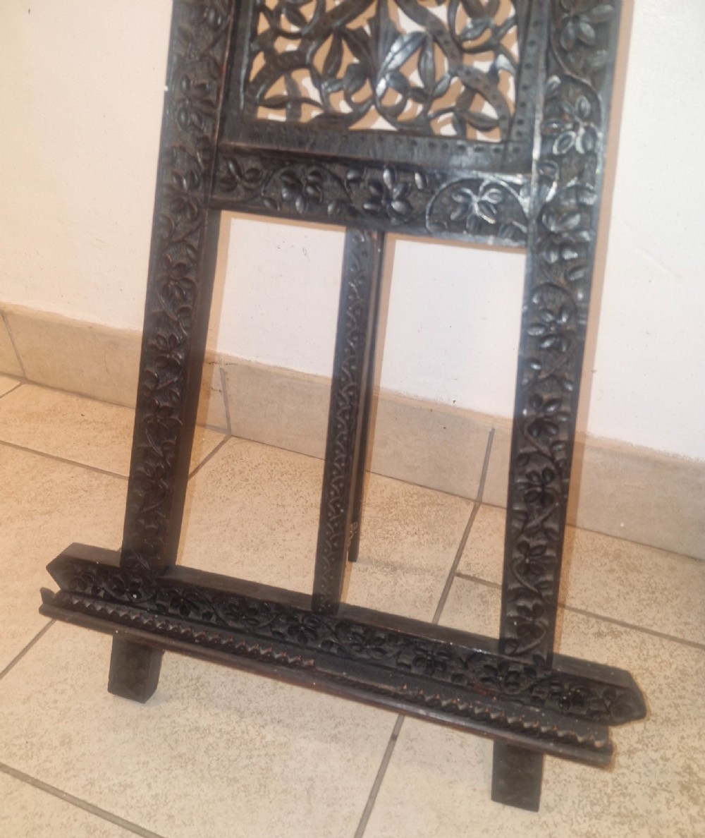 An intricate dark carved wooden tabletop display easel featuring pierced fretwork and floral motifs. View V