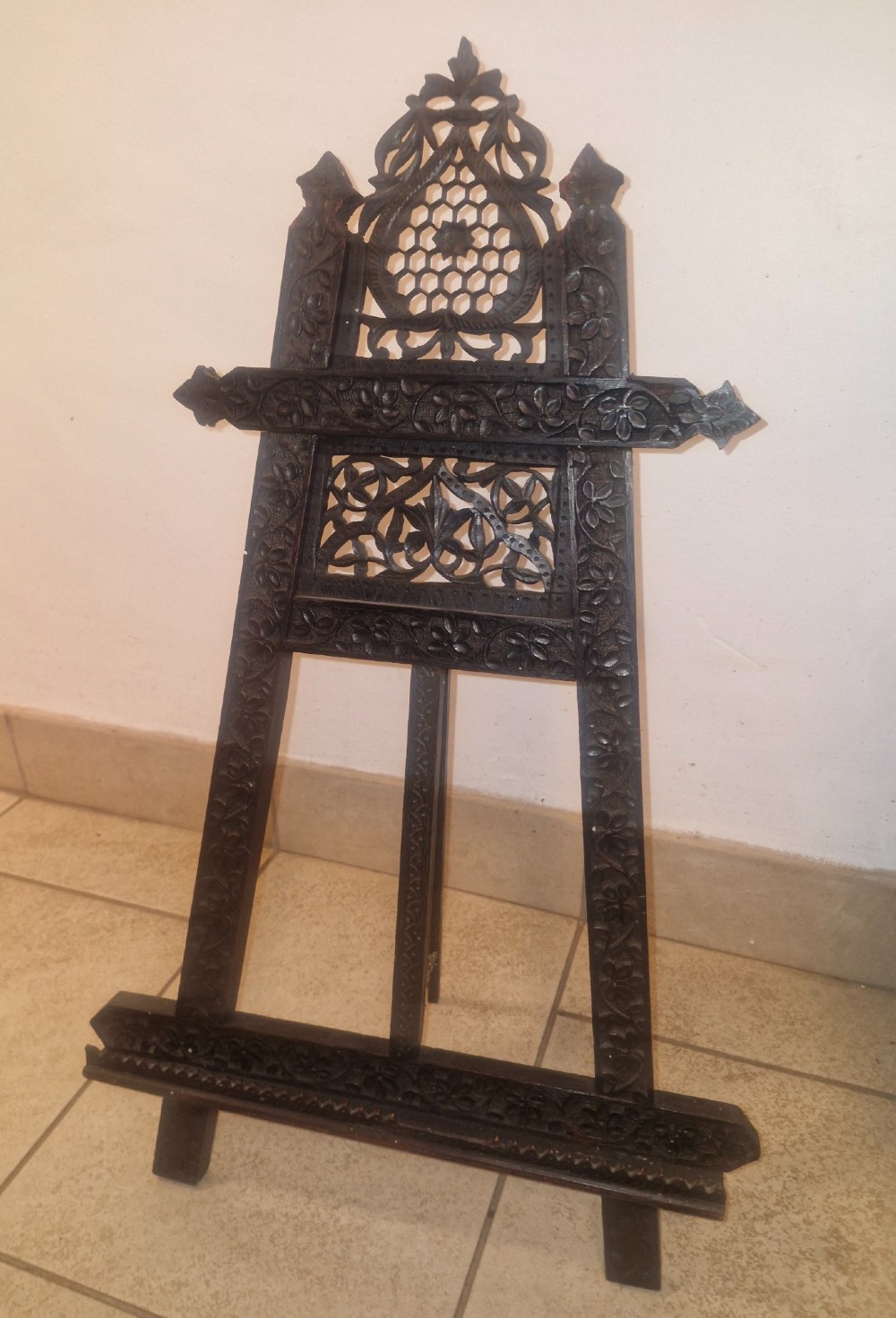 An intricate dark carved wooden tabletop display easel featuring pierced fretwork and floral motifs. View VIII