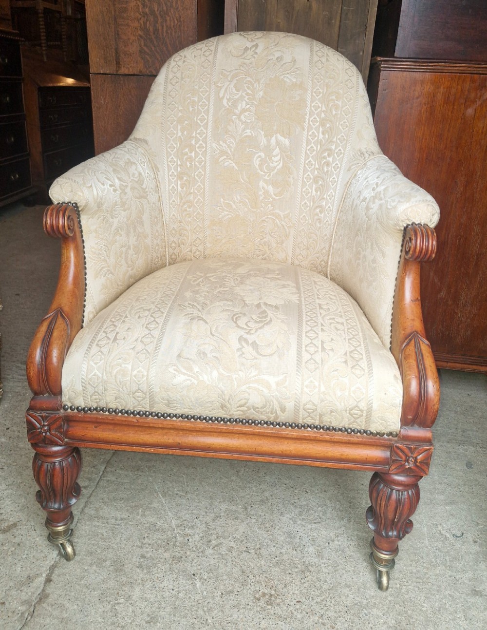 A Regency mahogany armchair upholstered in cream damask fabric with scroll arms and turned carved front legs on brass castors.