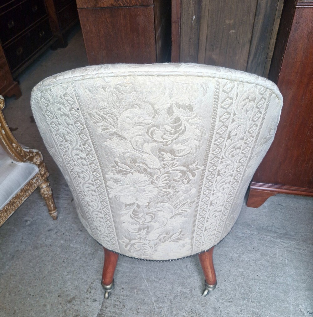 A Regency mahogany armchair upholstered in cream damask fabric with scroll arms and turned carved front legs on brass castors. View II
