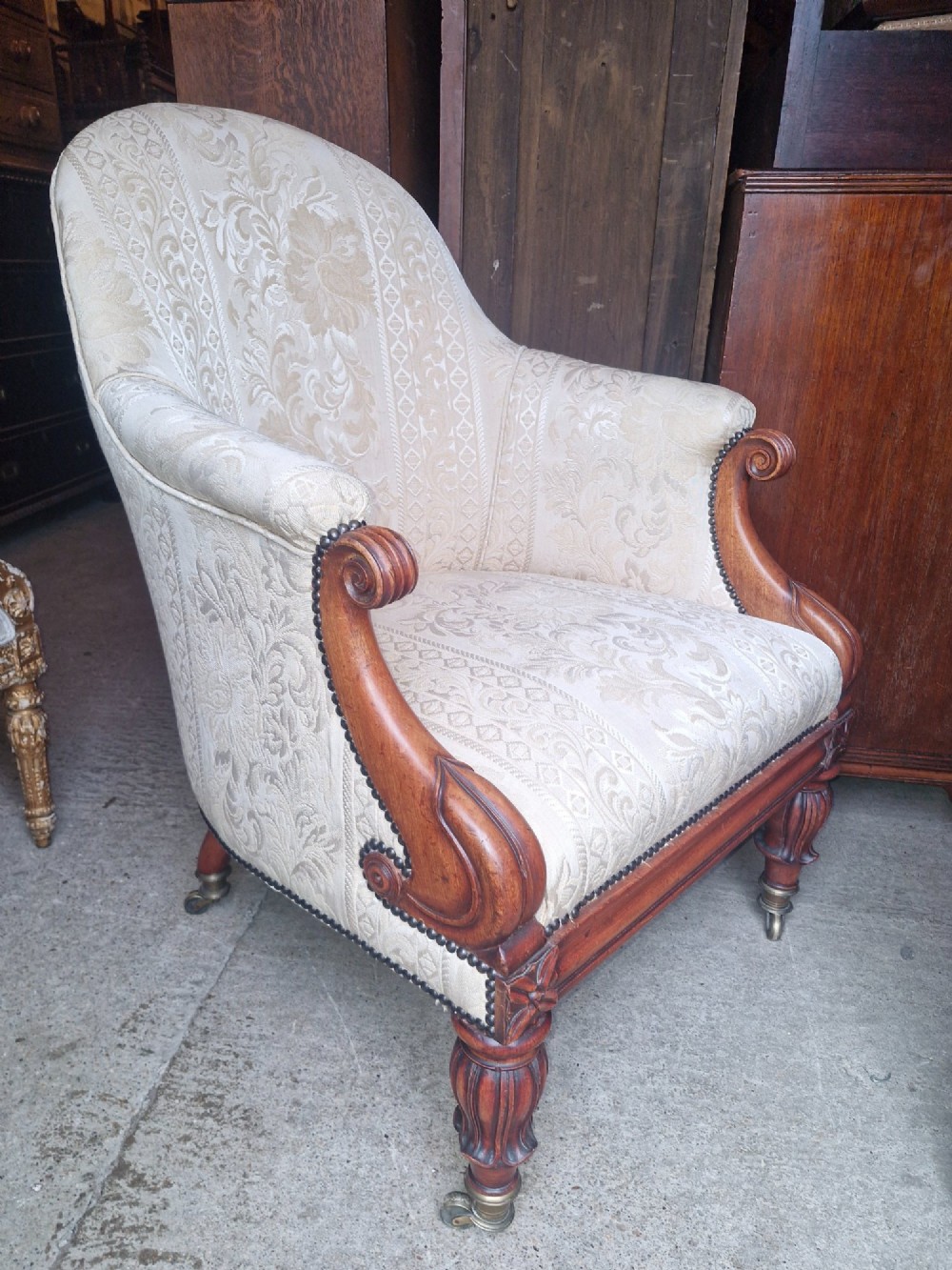 A Regency mahogany armchair upholstered in cream damask fabric with scroll arms and turned carved front legs on brass castors. View III
