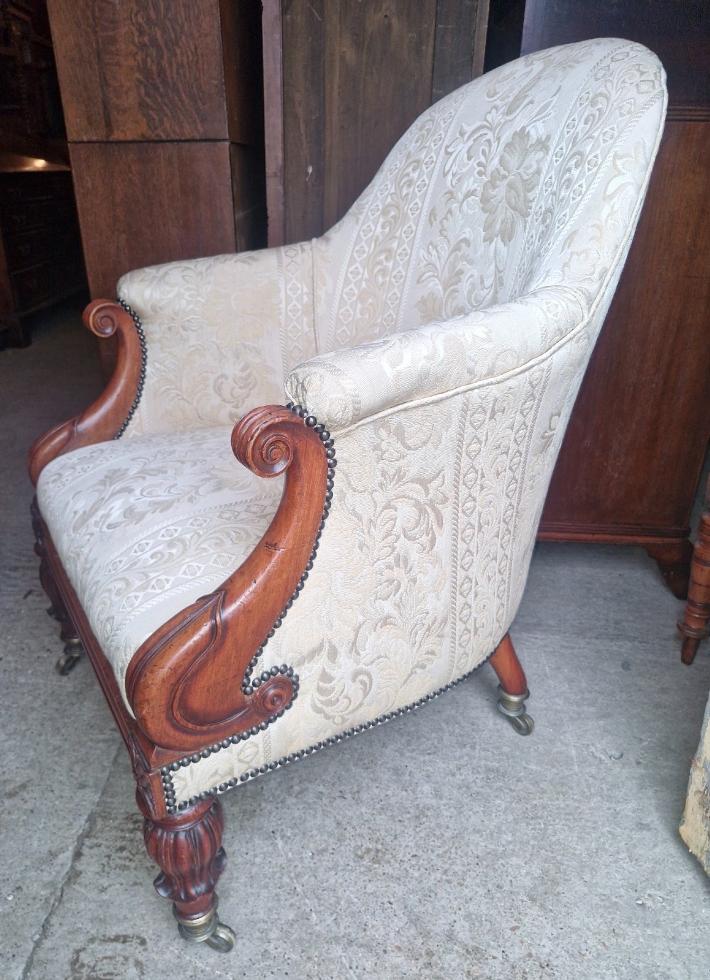 A Regency mahogany armchair upholstered in cream damask fabric with scroll arms and turned carved front legs on brass castors. View IV
