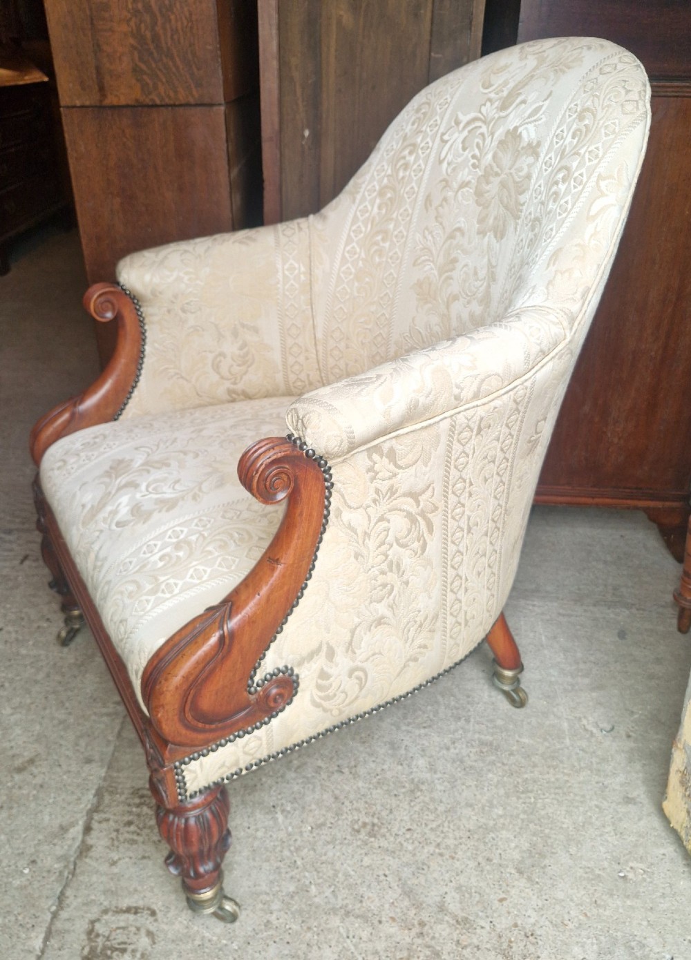 A Regency mahogany armchair upholstered in cream damask fabric with scroll arms and turned carved front legs on brass castors. View V