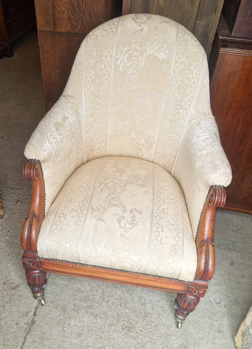 A Regency mahogany armchair upholstered in cream damask fabric with scroll arms and turned carved front legs on brass castors. View VI
