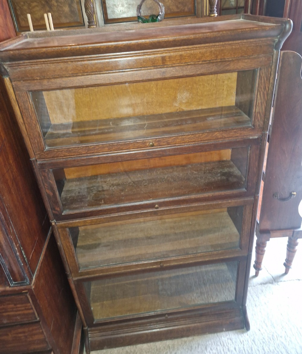 A four-tier oak sectional bookcase featuring glazed up-and-over doors and small brass knob handles. View IV