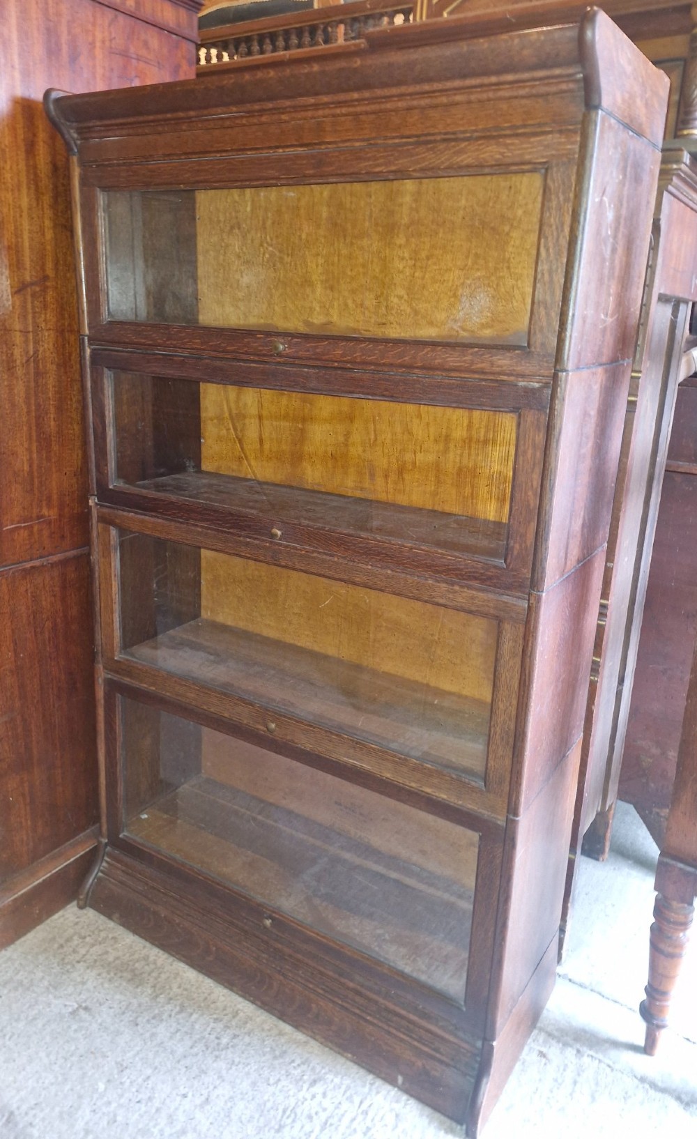 A four-tier oak sectional bookcase featuring glazed up-and-over doors and small brass knob handles. View VI