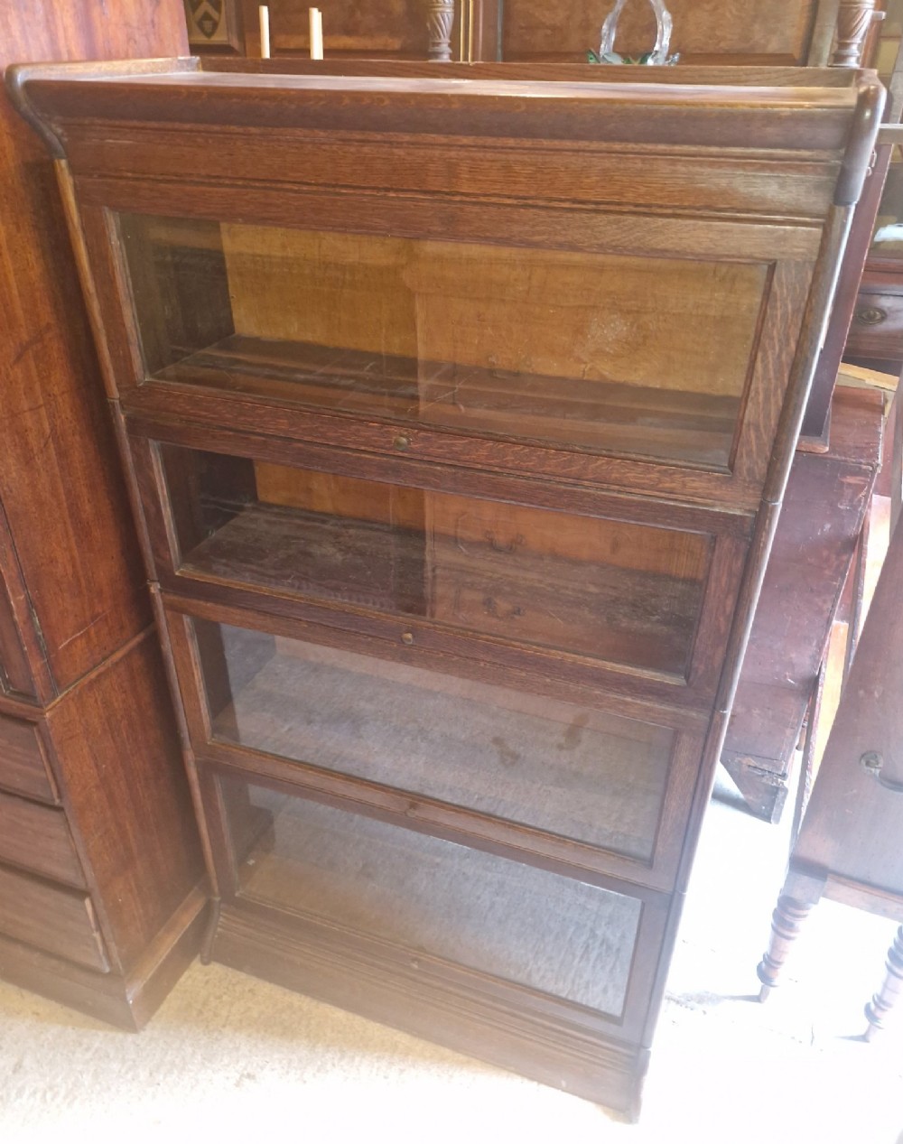 A four-tier oak sectional bookcase featuring glazed up-and-over doors and small brass knob handles. View VII