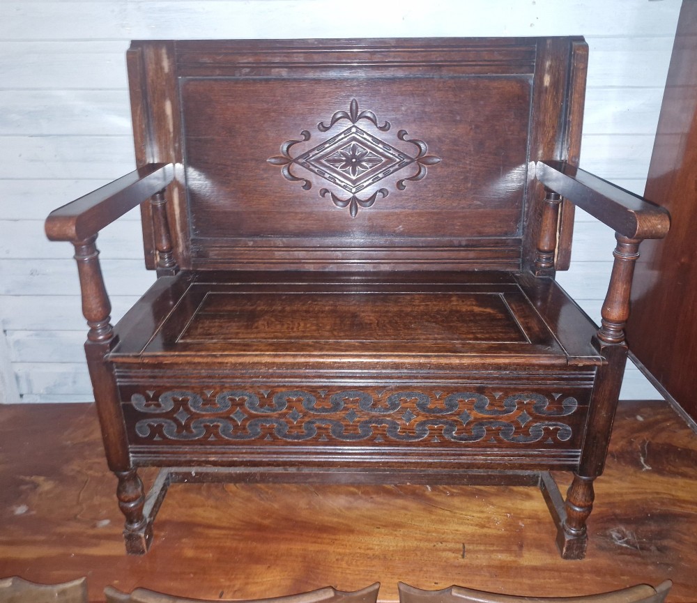 A dark oak monks bench featuring a carved diamond-patterned backrest, turned arm supports, carved front panel, and a lift-up seat. View V