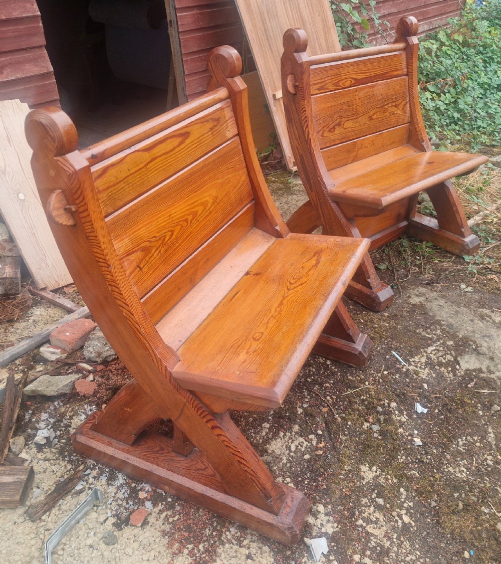 A pair of warm brown pitch pine hall seats with slatted backrests and carved Gothic side supports on plinth bases. View V
