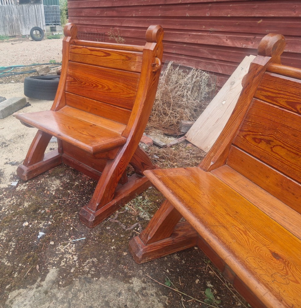 A pair of warm brown pitch pine hall seats with slatted backrests and carved Gothic side supports on plinth bases. View VI