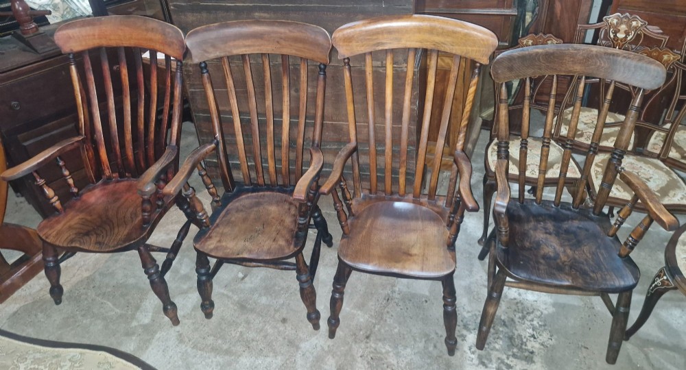 A set of four late Victorian wooden Windsor kitchen armchairs featuring spindle backs, shaped timber seats, turned legs, and stretchers.