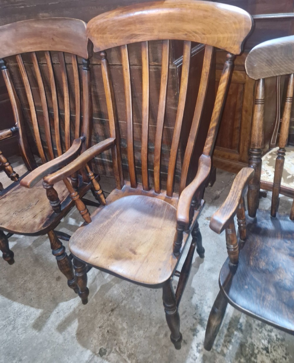 A set of four late Victorian wooden Windsor kitchen armchairs featuring spindle backs, shaped timber seats, turned legs, and stretchers. View IV
