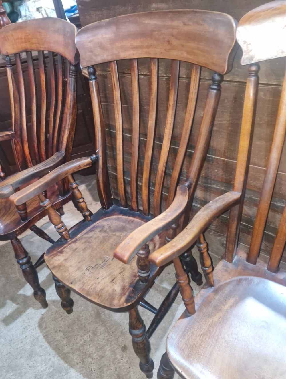 A set of four late Victorian wooden Windsor kitchen armchairs featuring spindle backs, shaped timber seats, turned legs, and stretchers. View VII