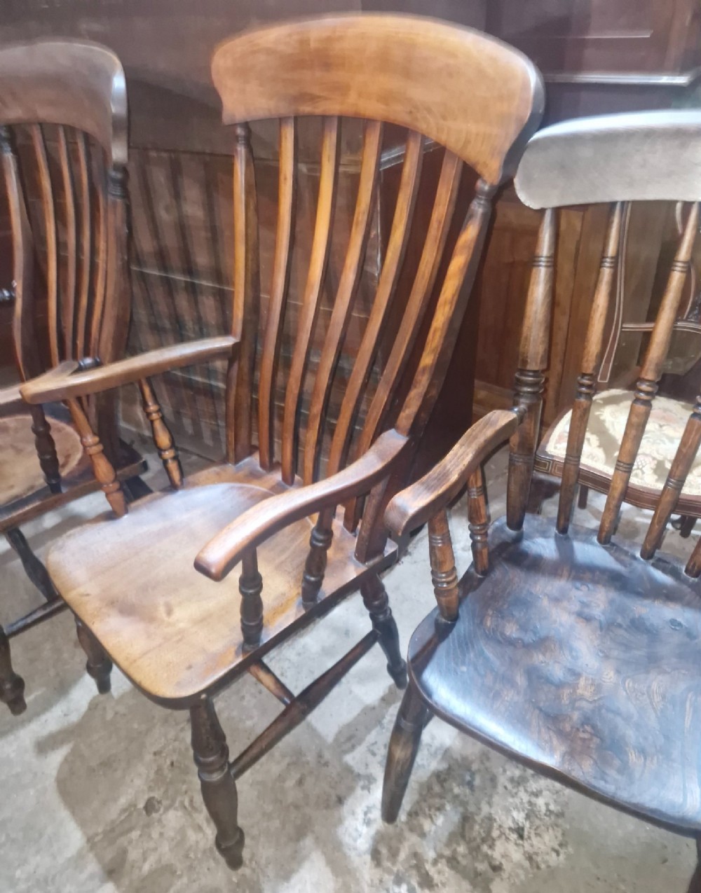 A set of four late Victorian wooden Windsor kitchen armchairs featuring spindle backs, shaped timber seats, turned legs, and stretchers. View IX