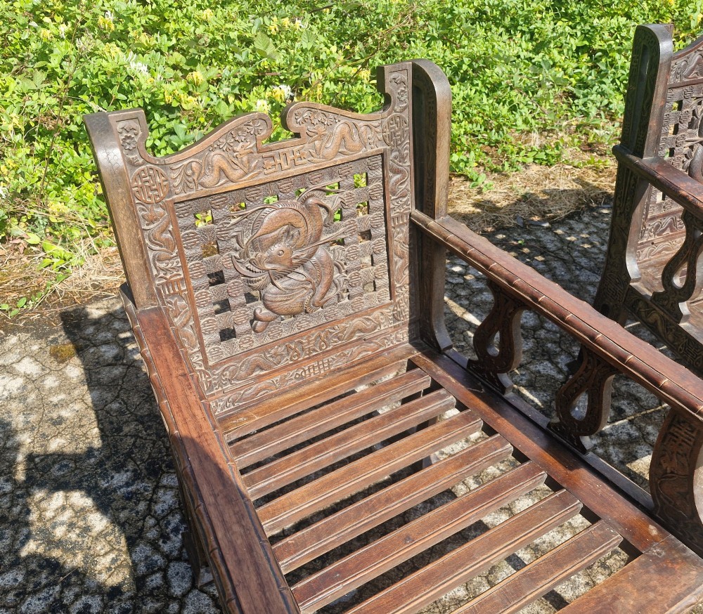 A three-piece dark carved teak seating suite comprising a double bench and two matching armchairs with intricate relief-carved backrests and slatted seats. View IV