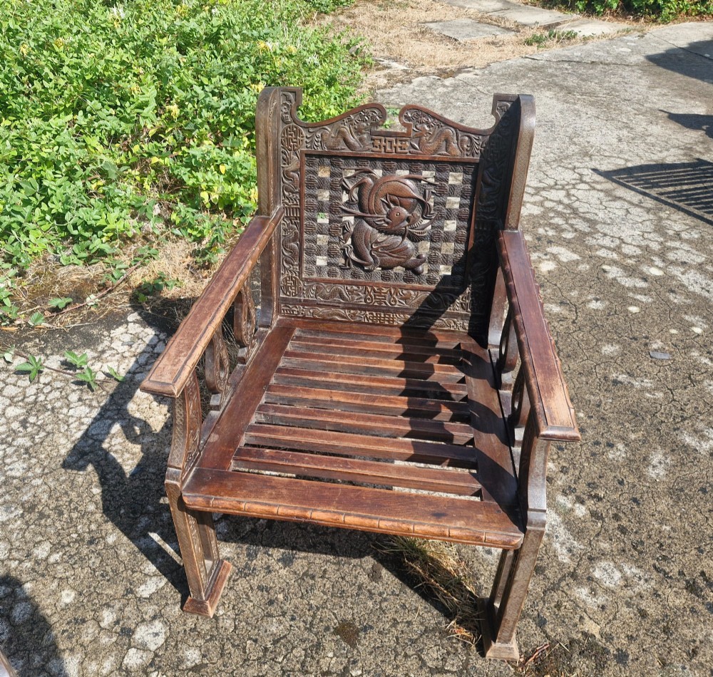 A three-piece dark carved teak seating suite comprising a double bench and two matching armchairs with intricate relief-carved backrests and slatted seats. View VII