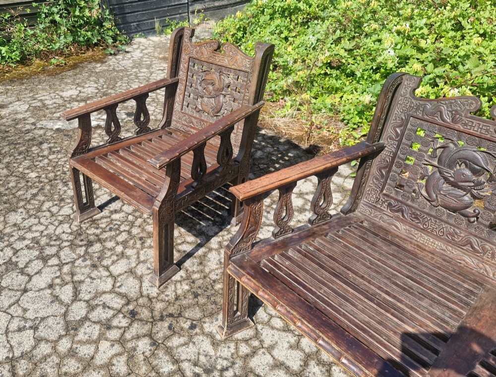 A three-piece dark carved teak seating suite comprising a double bench and two matching armchairs with intricate relief-carved backrests and slatted seats. View VIII