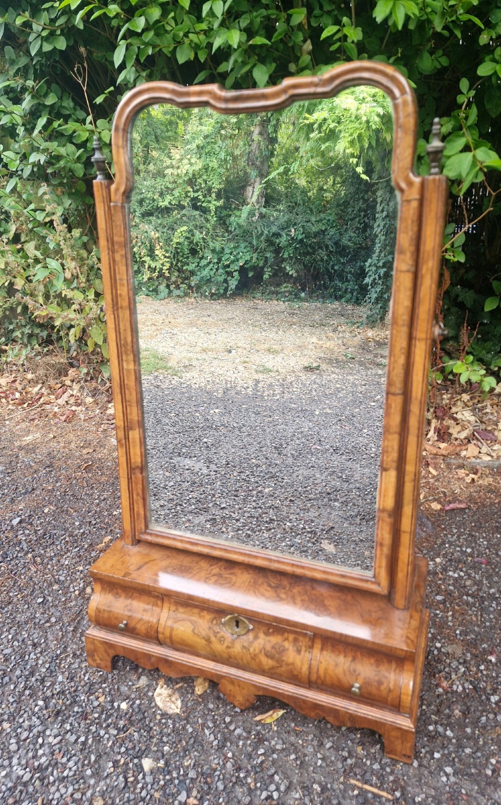 An 18th-century style walnut toilet mirror with a shaped frame supported on a box base containing a single drawer with brass hardware.