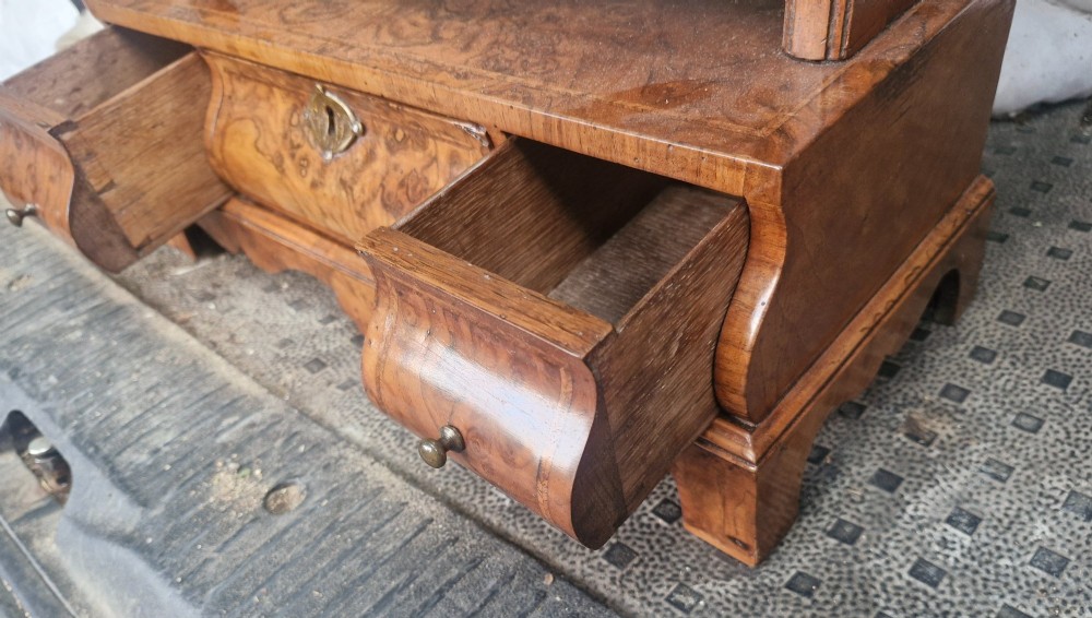An 18th-century style walnut toilet mirror with a shaped frame supported on a box base containing a single drawer with brass hardware. View II