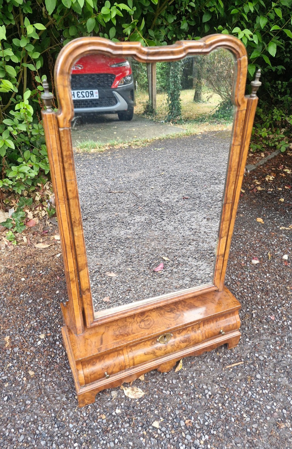 An 18th-century style walnut toilet mirror with a shaped frame supported on a box base containing a single drawer with brass hardware. View IV