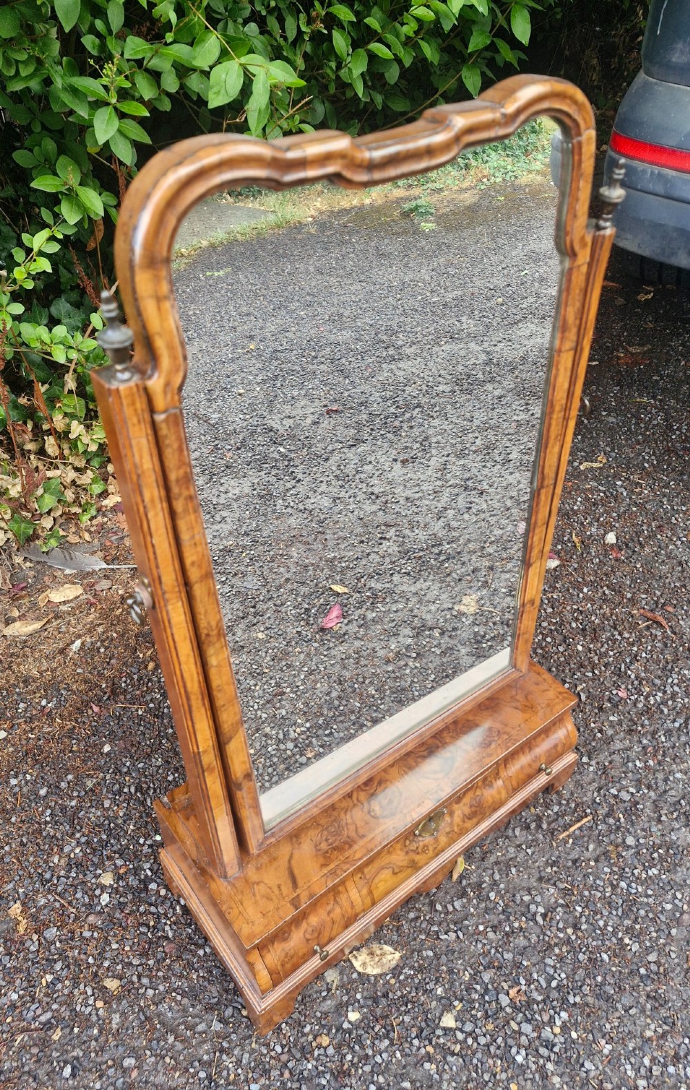 An 18th-century style walnut toilet mirror with a shaped frame supported on a box base containing a single drawer with brass hardware. View VI