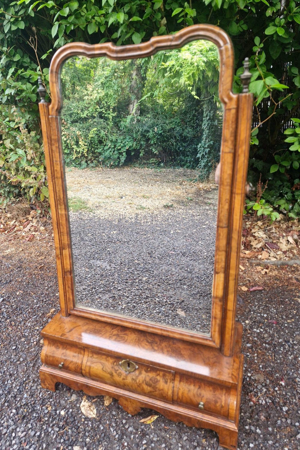 An 18th-century style walnut toilet mirror with a shaped frame supported on a box base containing a single drawer with brass hardware. View VIII