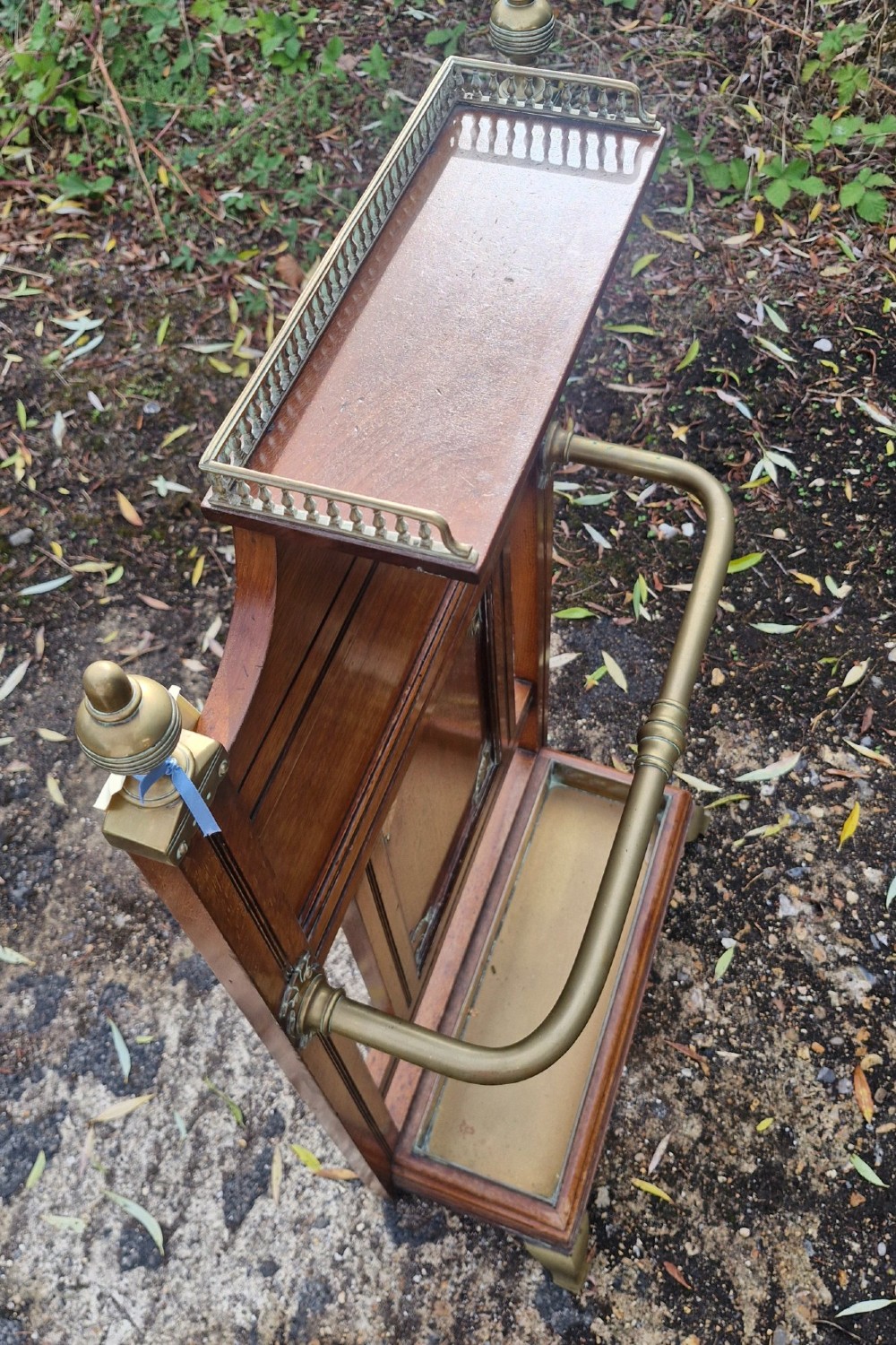 Late Victorian wooden stick stand featuring turned brass finials, a galleried top shelf, a brass retaining rail, and a removable drip tray. View II