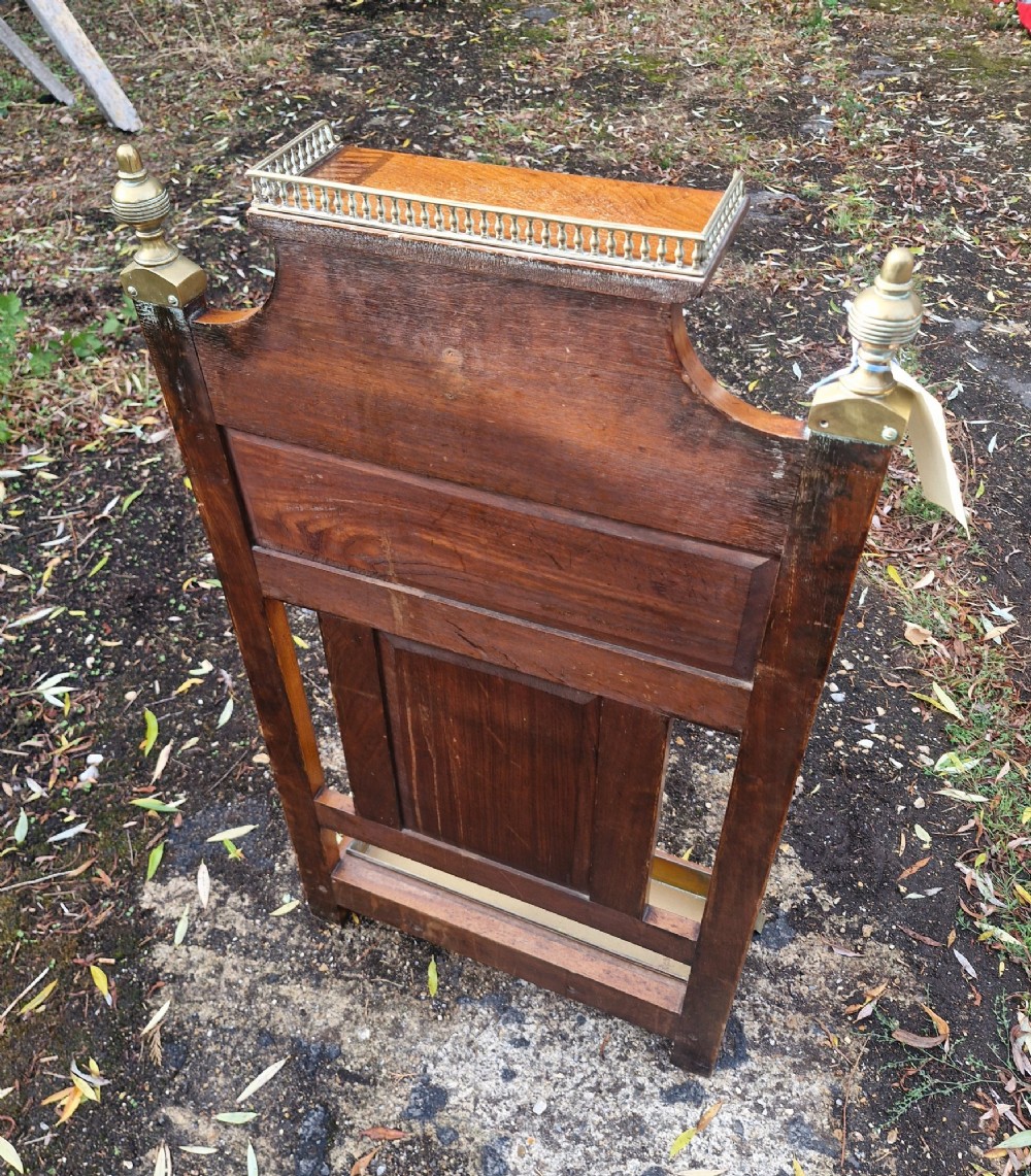 Late Victorian wooden stick stand featuring turned brass finials, a galleried top shelf, a brass retaining rail, and a removable drip tray. View IV