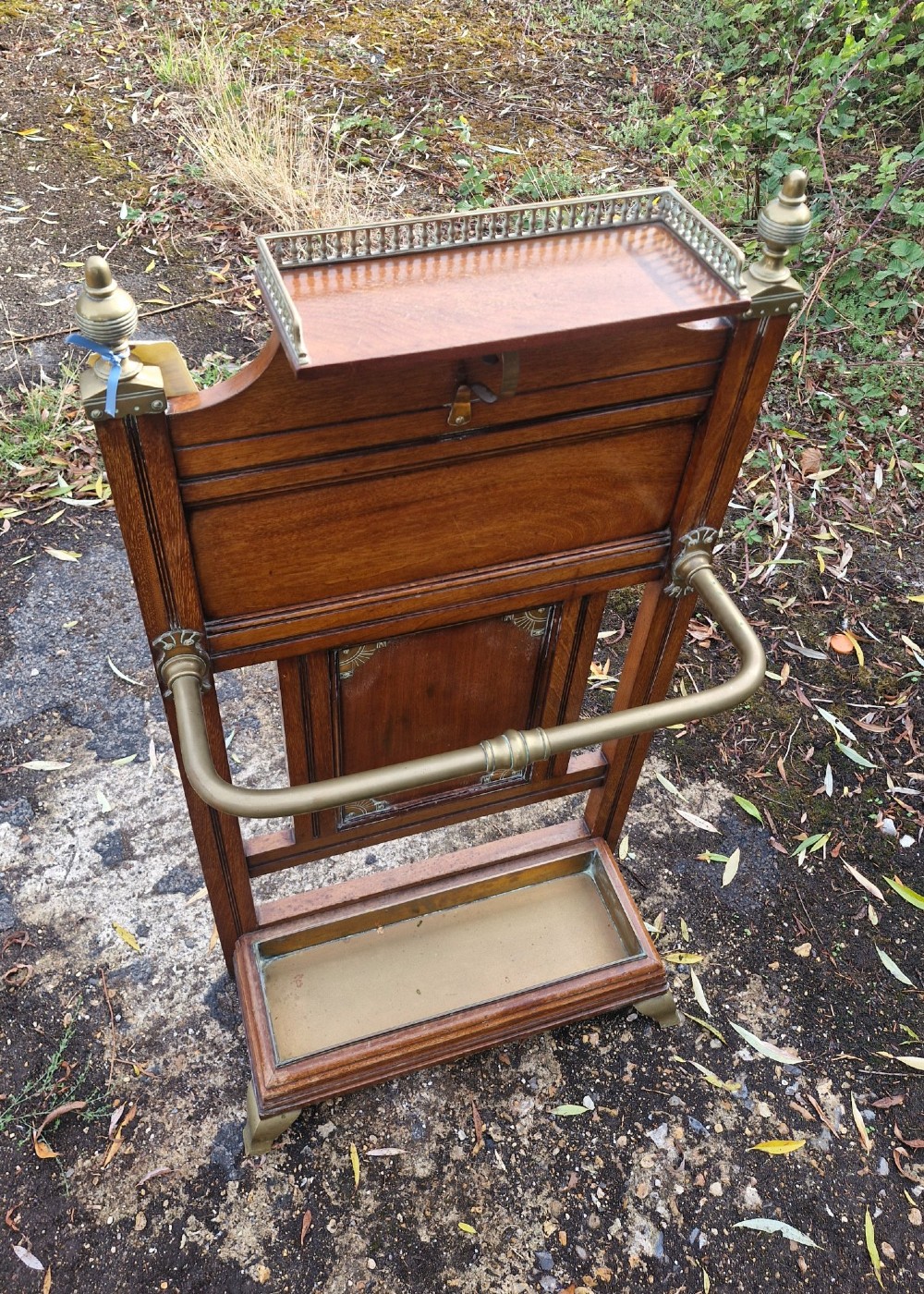 Late Victorian wooden stick stand featuring turned brass finials, a galleried top shelf, a brass retaining rail, and a removable drip tray. View V