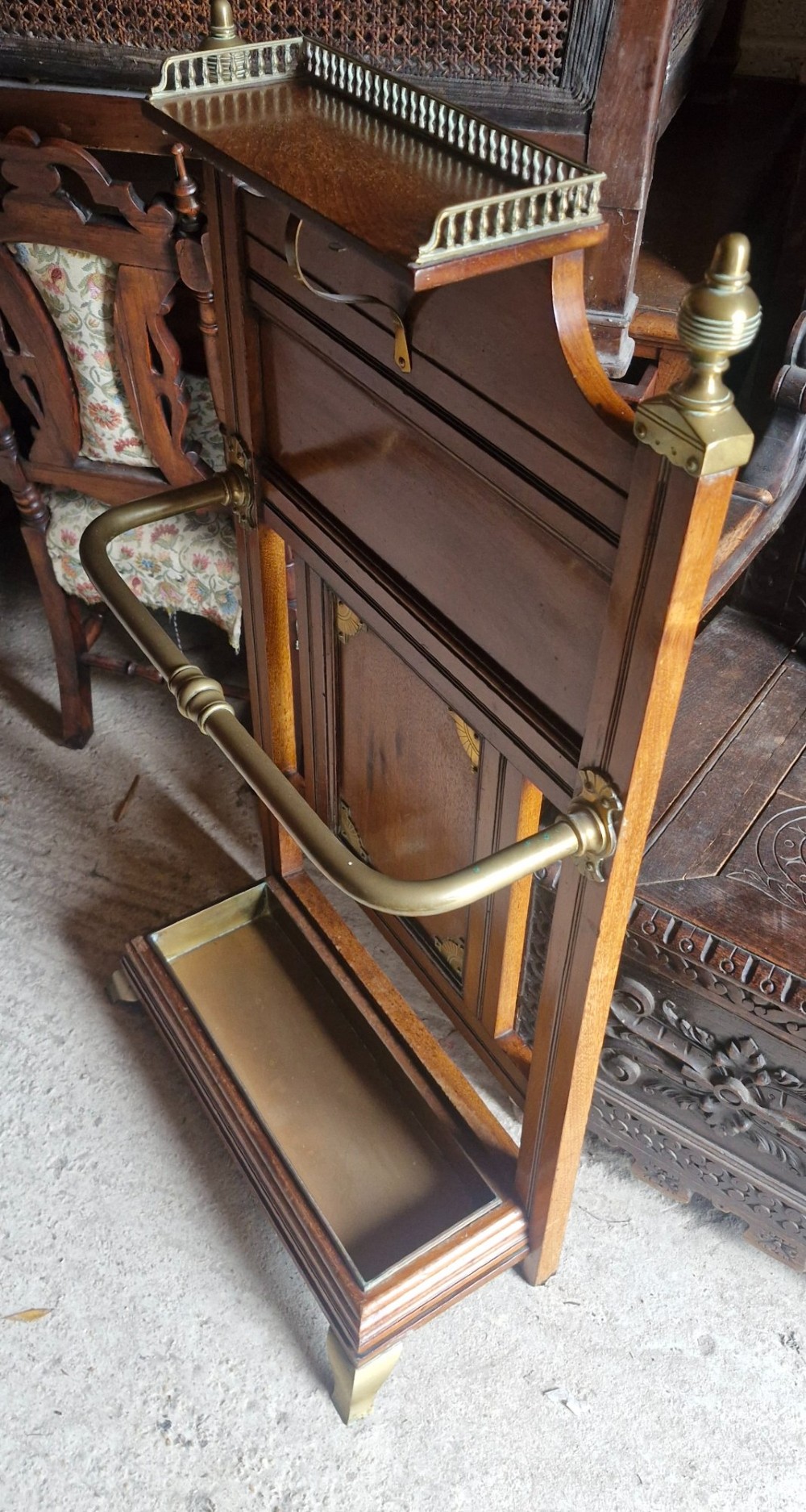 Late Victorian wooden stick stand featuring turned brass finials, a galleried top shelf, a brass retaining rail, and a removable drip tray. View VI