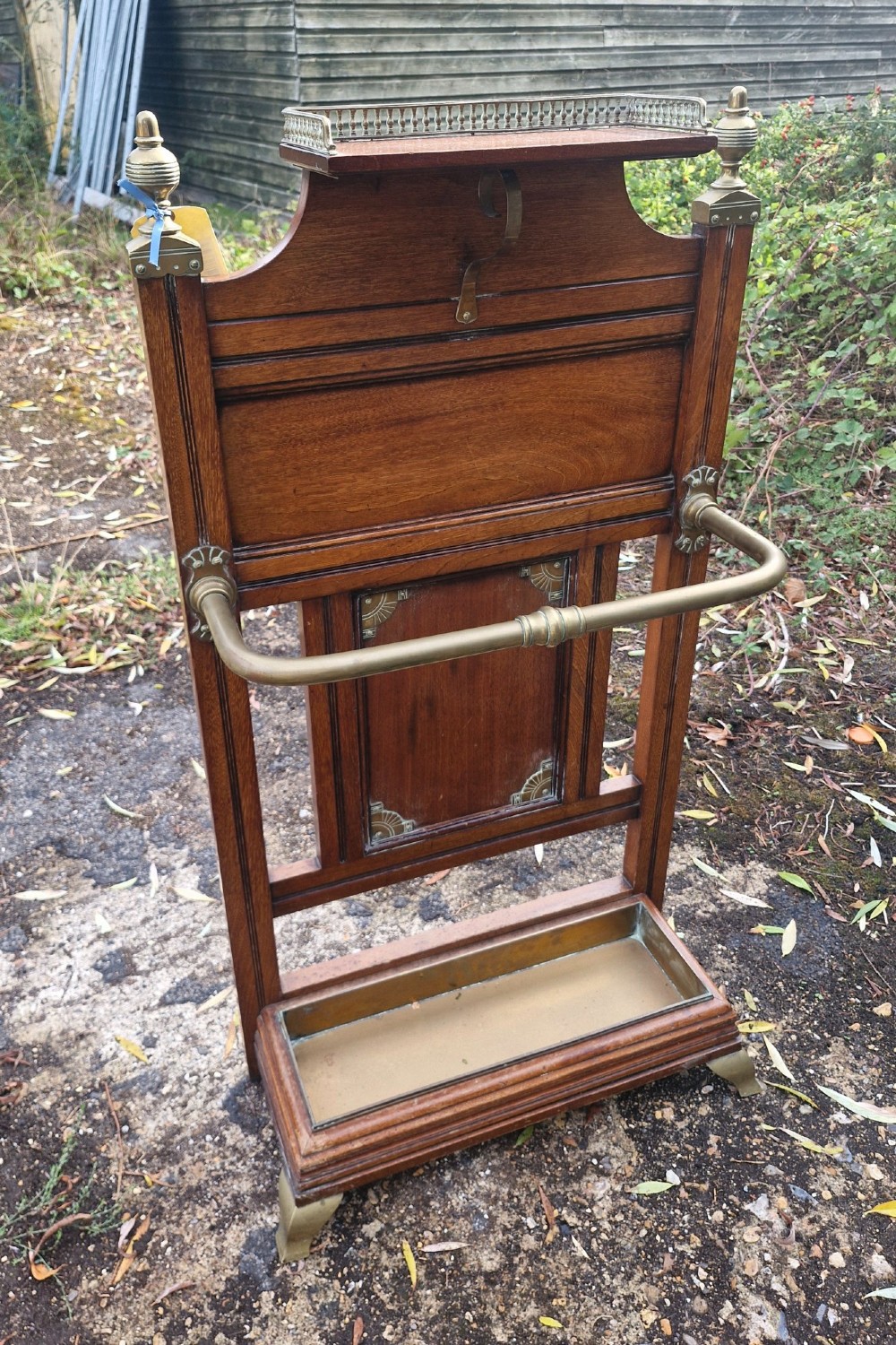 Late Victorian wooden stick stand featuring turned brass finials, a galleried top shelf, a brass retaining rail, and a removable drip tray. View VII