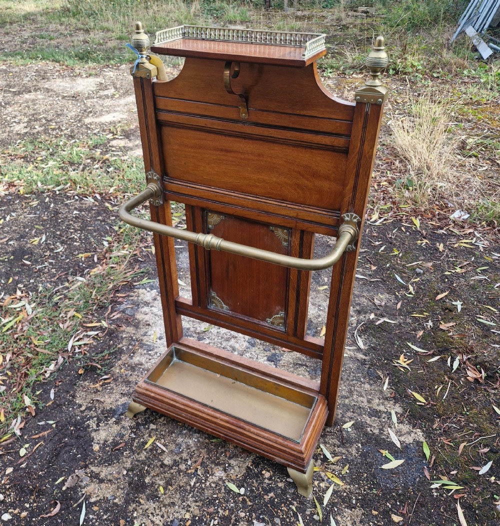 Late Victorian wooden stick stand featuring turned brass finials, a galleried top shelf, a brass retaining rail, and a removable drip tray. View VIII
