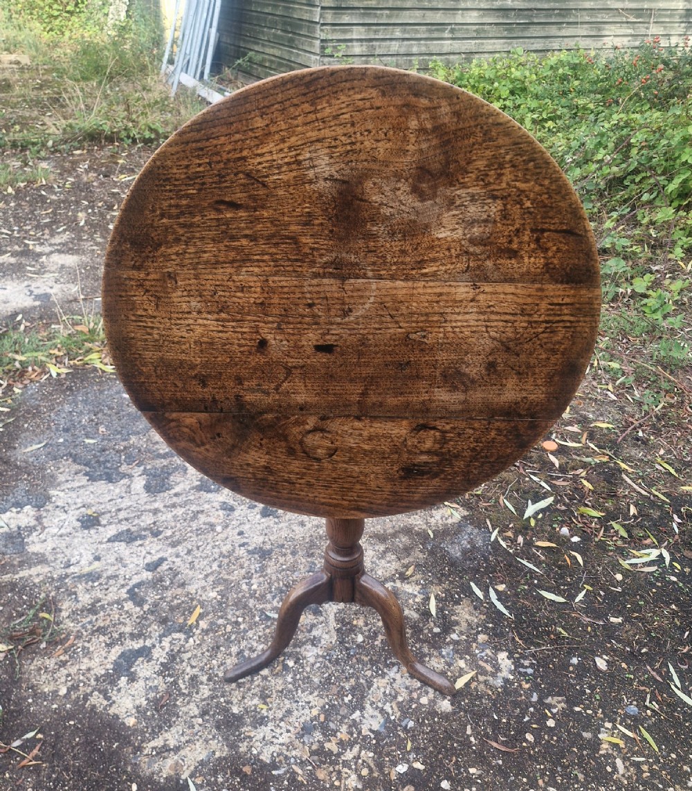 A late Georgian oak tripod table with a circular tilt-top surface positioned vertically, supported by a turned column and three cabriole legs.