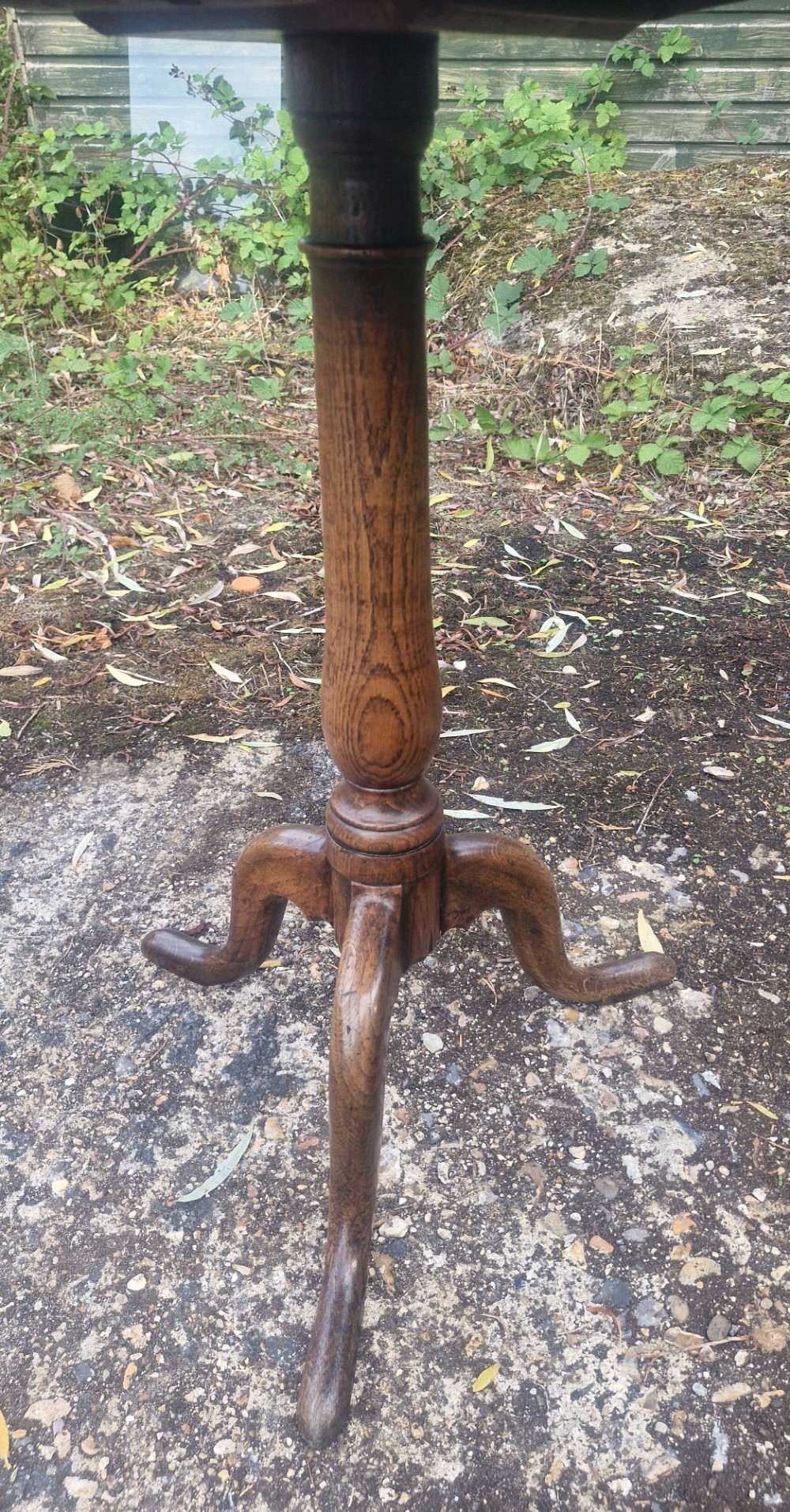 A late Georgian oak tripod table with a circular tilt-top surface positioned vertically, supported by a turned column and three cabriole legs. View II
