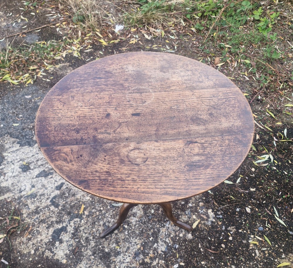 A late Georgian oak tripod table with a circular tilt-top surface positioned vertically, supported by a turned column and three cabriole legs. View IV